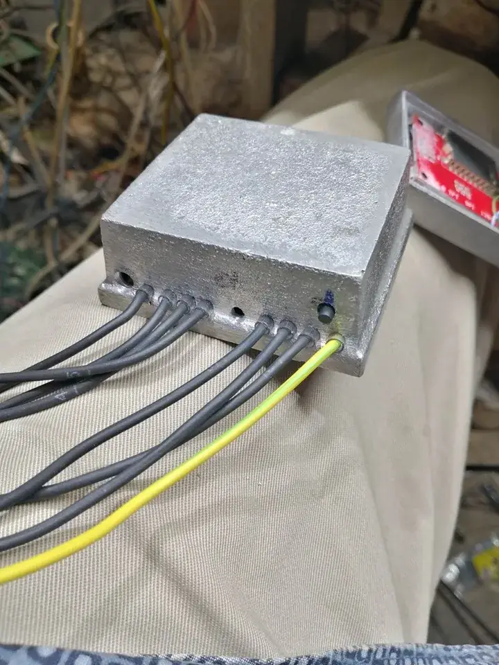 La caja de aluminio cerrada y apoyada de canto, con ocho cables grises y uno amarillo y verde saliendo por agujeros en el lateral