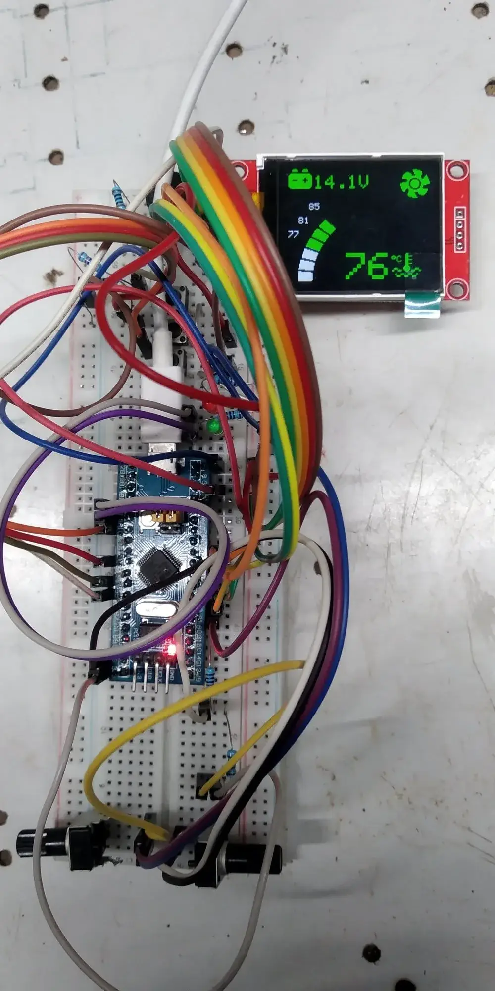 Pantalla TFT a color montada junto a una protoboard con la placa STM32 y cables de colores: marca 14,1 V arriba con un icono de batería verde, 76 grados en verde y grande, y una barra vertical de segmentos a media altura