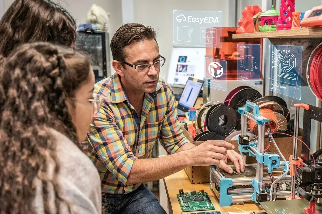 Instructor señalando una impresora 3D a dos estudiantes en un fablab, con placas PCB y un Arduino Uno sobre la mesa y paneles flotantes de EasyEDA y diseño de PCB