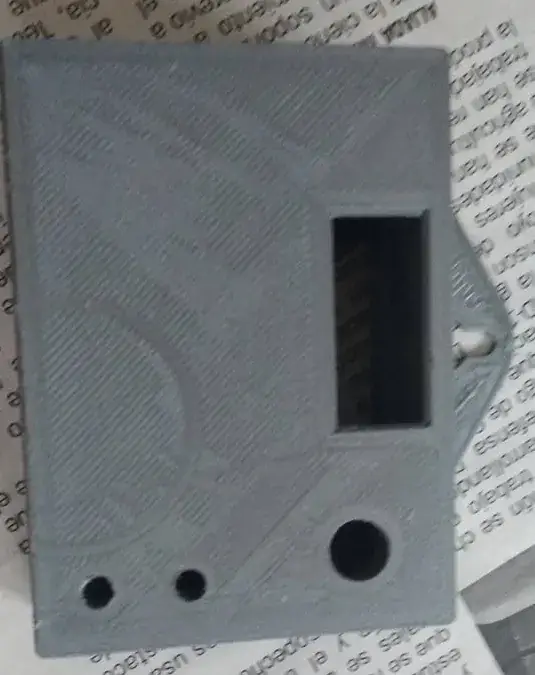 Caja impresa en 3D gris, cerrada, con una ventana rectangular para la pantalla OLED, dos agujeros pequeños para los LED y uno grande abajo