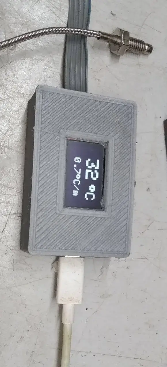 Caja impresa en 3D cerrada con la pantalla OLED marcando 32 grados Celsius y, al lado, 0,7 grados Celsius por minuto; arriba, el termopar con su sonda de rosca y el cable trenzado